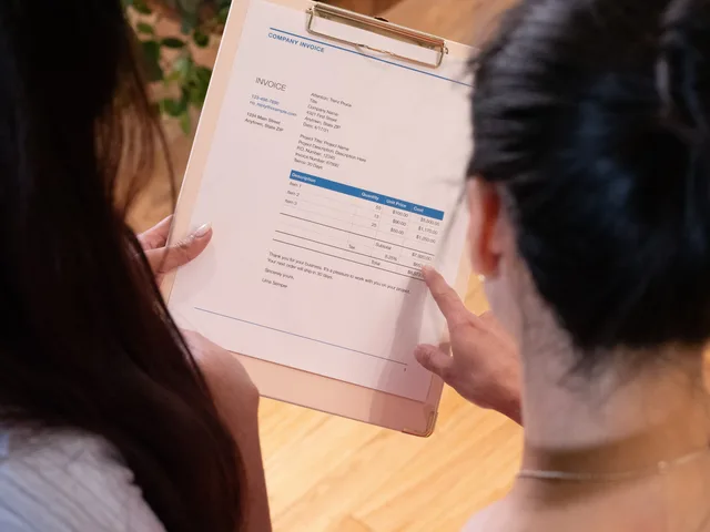 Two individuals reviewing an invoice together in a modern office setting. Sådan udsteder du en faktura efter dansk lov