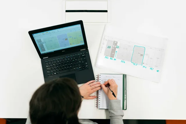 A person working on a laptop, making notes from digital data and charts in an office setting. Webshop til små virksomheder: Sådan kommer du i gang